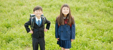 小学生の男の子と女の子が生い茂る黄緑色の草の上に立ってこちらに微笑んでいる写真